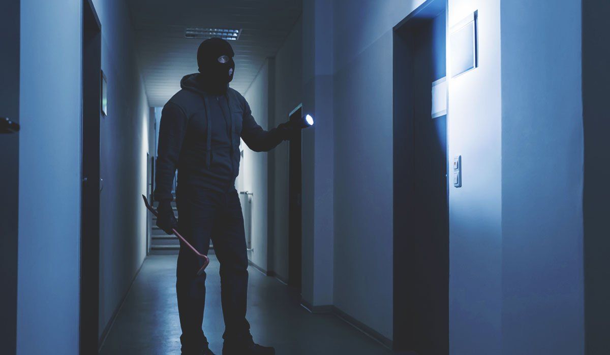Intruder with a crowbar in a dark commercial hallway, the break-in a monitored burglar alarm is built to stop